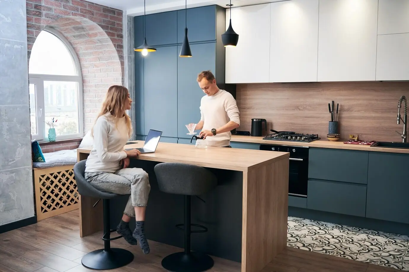 A man and a woman working on a laptop at home in a modern kitchen.